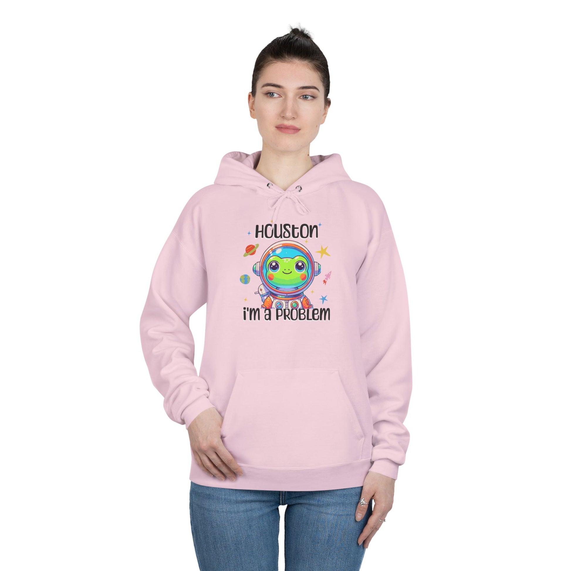 a woman wearing a light pink colored hoodie with graphic of a cute astronaut frog in a spacesuit, ready for an interstellar adventure. The design showcases the frog as a space cadet, radiating charm and joy, perfect for spreading smiles across the galaxy