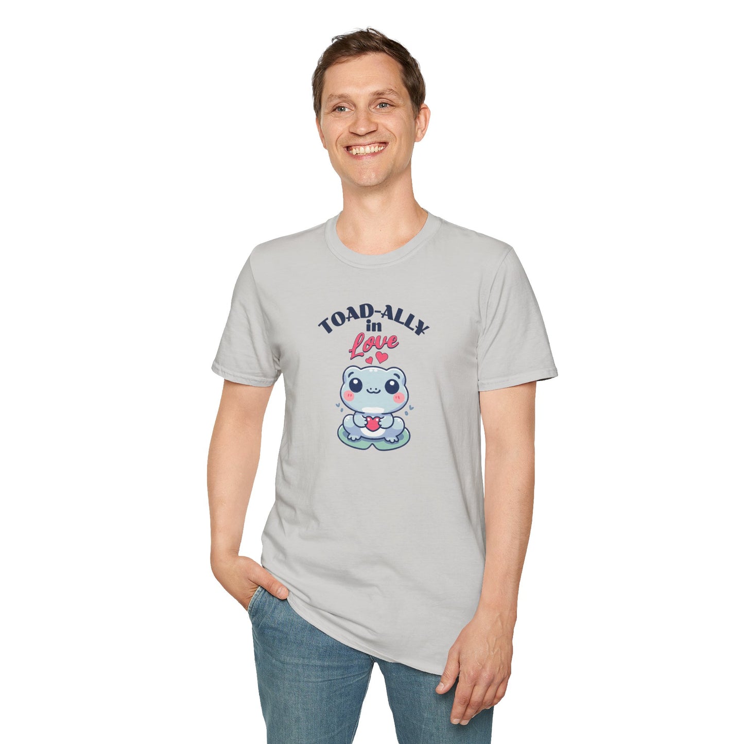 a man wearing a cartoonish blue frog with a cheerful expression holds a small red heart in its hands. The design is printed on a ice grey T-shirt and features the playful phrase 'Leap into Love!' adding a charming and romantic vibe.