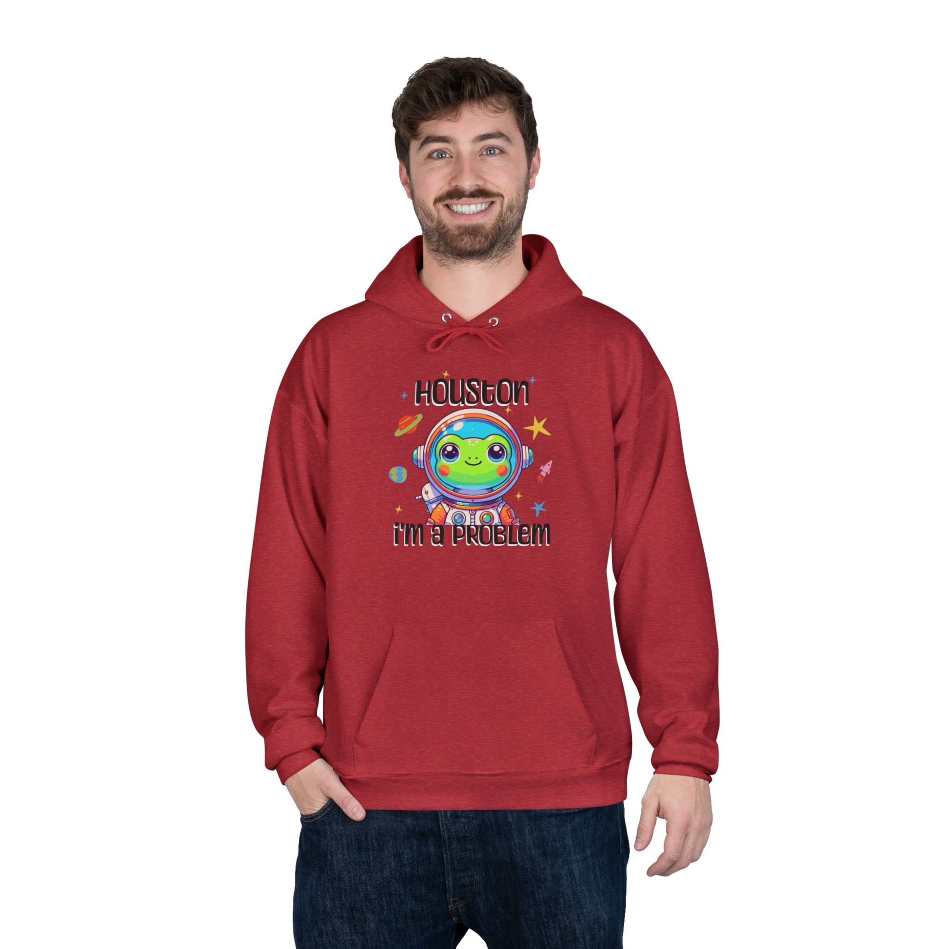 a man wearing a heather red colored hoodie with graphic of a cute astronaut frog in a spacesuit, ready for an interstellar adventure. The design showcases the frog as a space cadet, radiating charm and joy, perfect for spreading smiles across the galaxy