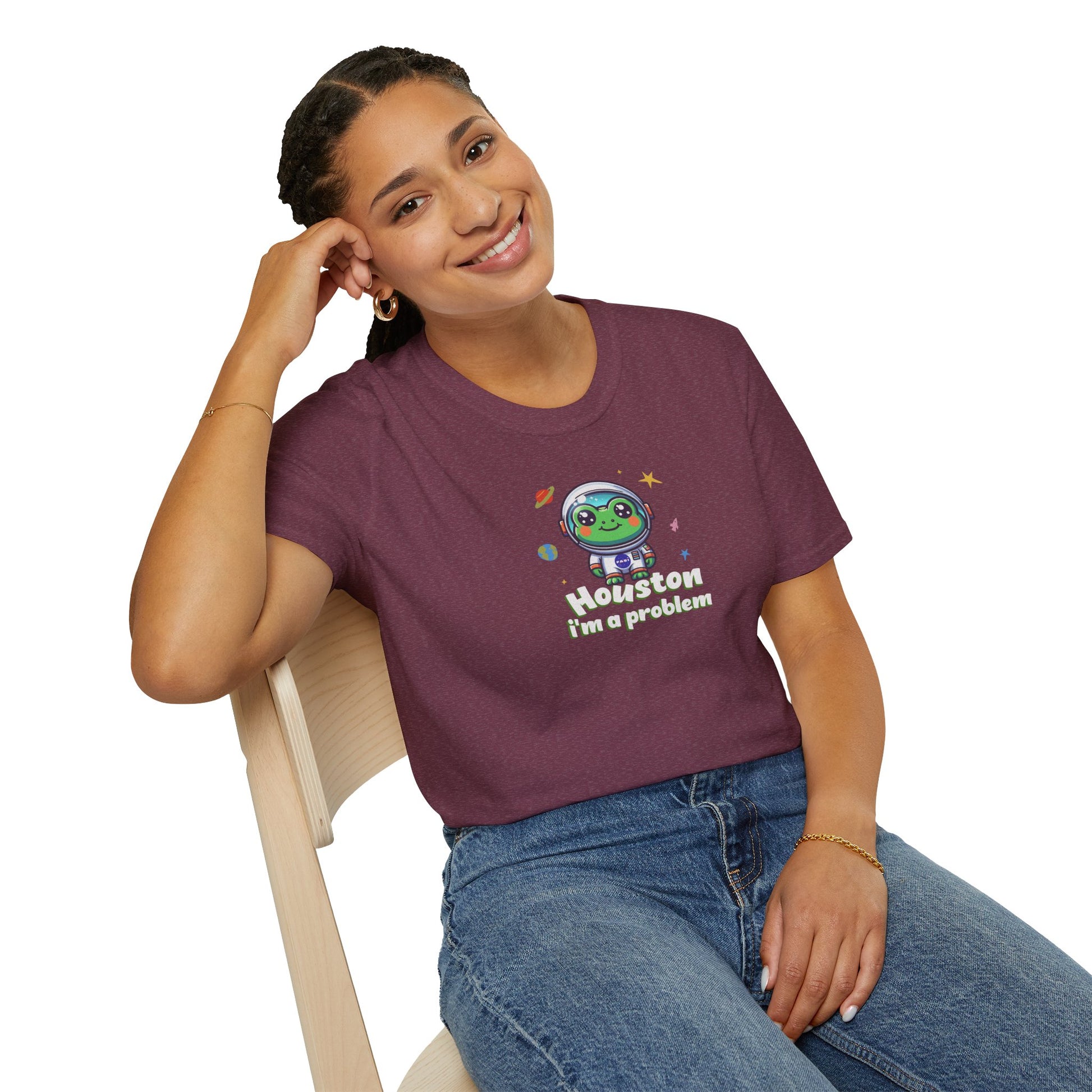 a woman wearing a heather maroon colored t-shirt with graphic of a cute astronaut frog in a spacesuit, ready for an interstellar adventure. The design showcases the frog as a space cadet, radiating charm and joy, perfect for spreading smiles across the galaxy