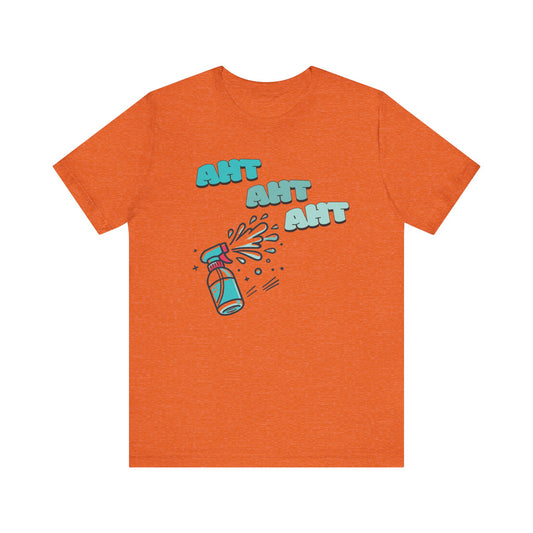 A spray bottle shooting three squirts of water, each squirt accompanied by the playful text 'Aht Aht Aht.' The design is printed on a heather orange T-shirt, adding a humorous and cheeky vibe, perfect for warding off unwanted behavior with a lighthearted message.