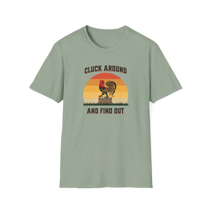 Sage colored t-shirt featuring a red and black rooster standing on a brown tree stump on green grass, set against a retro red-to-orange sunset background with the text 'Cluck Around and Find Out'.